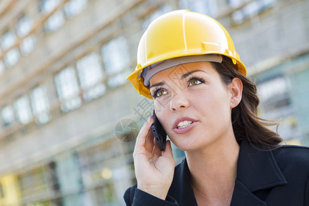 年轻专业女承包商使用手机在对接地点戴硬帽图片