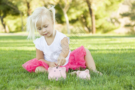 可爱的小女孩玩得开心与她的大和小猪银行外面的草地上图片
