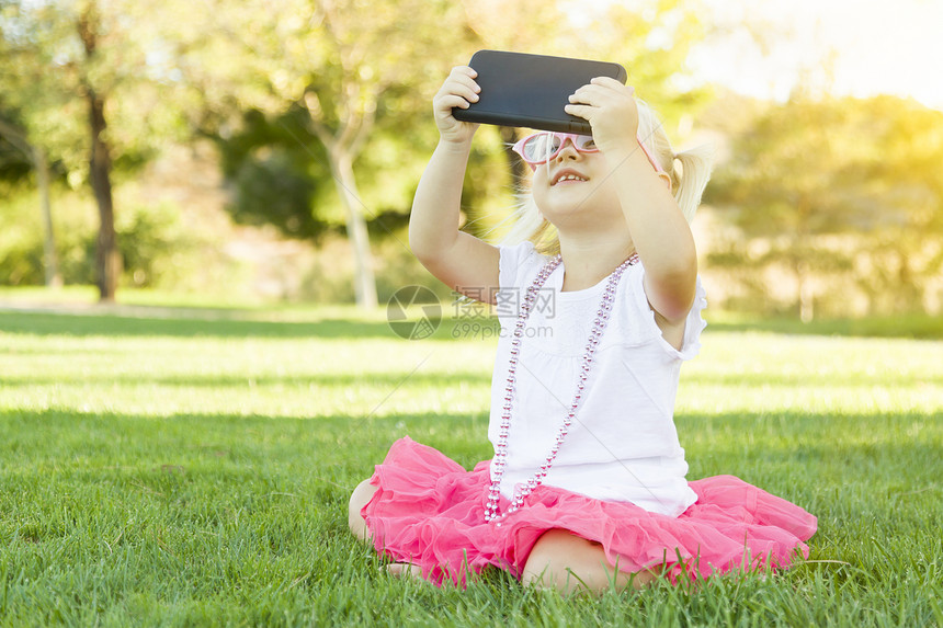 坐在草地上的可爱小女孩用手机拍自图片