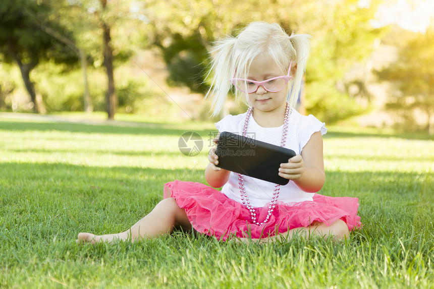 坐在草地上玩手机的可爱小女孩图片
