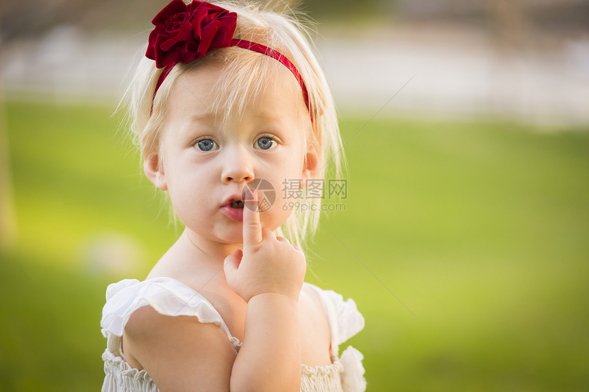美丽的可爱小女孩她手指在嘴上穿着白色的裙子在草地上图片