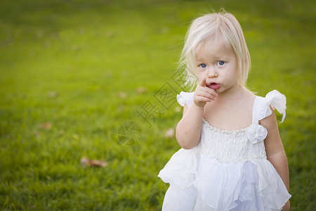可爱的小女孩指着摄影机穿白色衣服在草地上图片