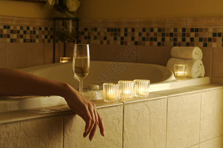 在泡浴中美丽的女人周围有闪亮的葡萄酒和蜡烛高清图片
