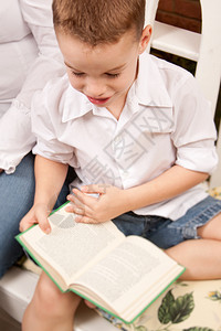 可爱的小男孩在妈旁边的室内读他书图片