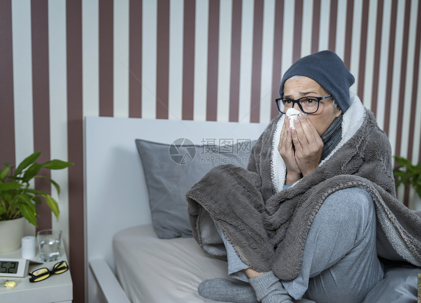 发烧的老年女人吹鼻涕坐在床上图片