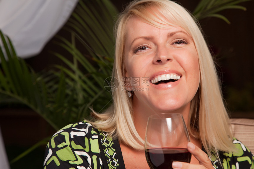 美丽的金发女在晚间社交聚会上微笑喝着葡萄酒图片