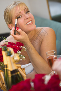 迷人的金发女郎在香槟和玫瑰边的镜子上化妆图片