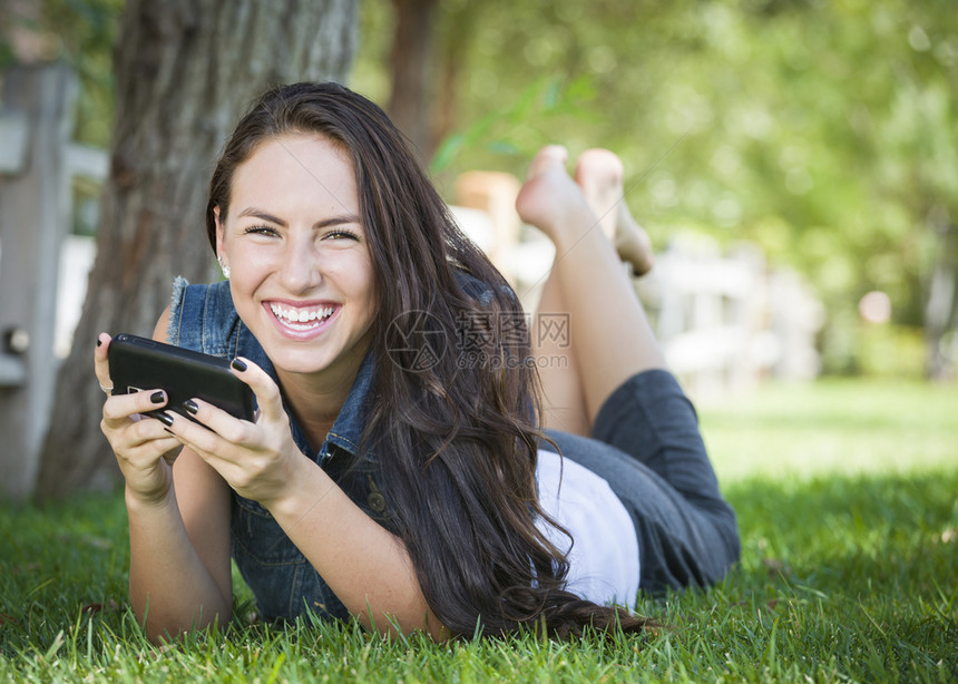 年轻女在外边的手机上发短信躺在草地上图片