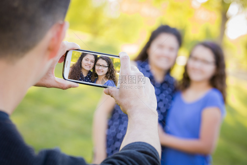 男人在公园外拍摄妻子和女儿的手机照片图片