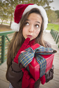 穿着圣诞帽子佩戴包装礼物并在外面鞠躬的漂亮喜悦微笑的女人图片