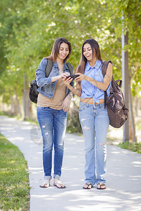 成人混血青年姐妹在公园边散步边玩手机图片