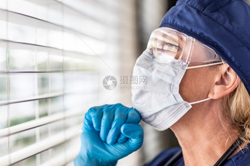 女医生或护士在窗户上休息时戴着医疗面罩和护目镜图片