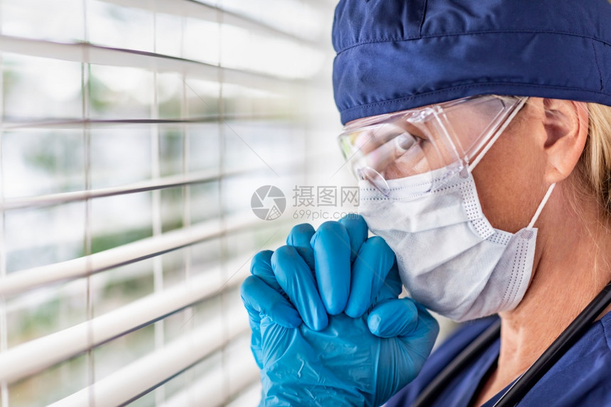 身戴医疗面罩和护目镜的女医生或护士在窗户上休息时身着重力图片