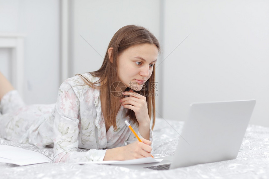 工作使用笔记本电脑在家里卧室做笔记自由职业者写字打女孩检查社会应用程序通信和技术概念美丽的年轻女工作通信和技术概念图片