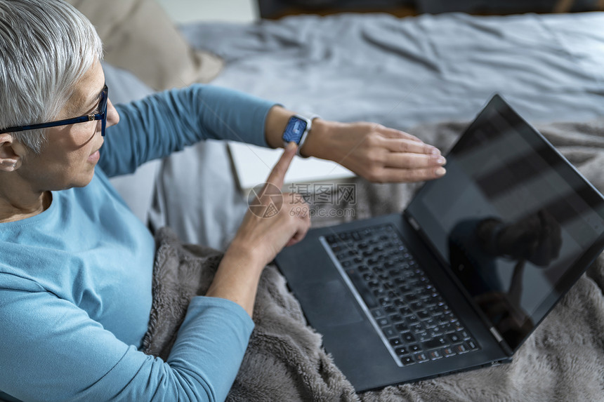 在床上有智能手表和笔记本电脑的妇女担心她睡眠质量图片