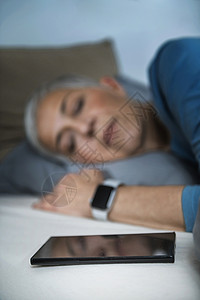 大咖来袭睡眠应用高科技流经的老年妇女睡在床上使用智能电话和手表来改善她的睡眠习惯背景