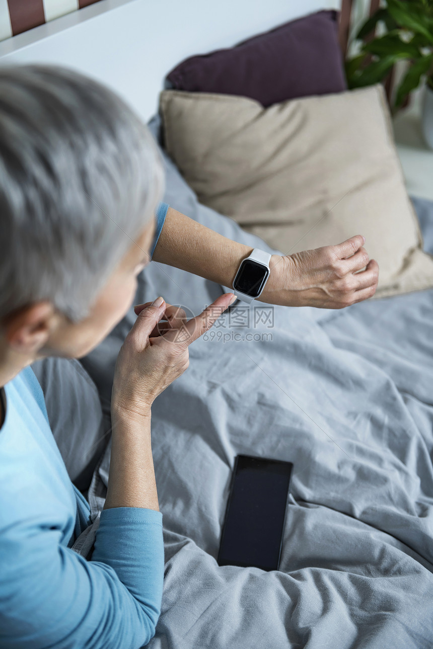 睡用软件床上的老年妇女早上醒来后检查智能手表睡眠跟踪器图片