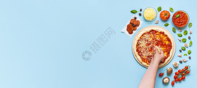 蓝色手把妇女手把奶酪放在比萨上顶层视图由厨师一步地做比萨饼上面是蓝桌的比萨饼成分背景