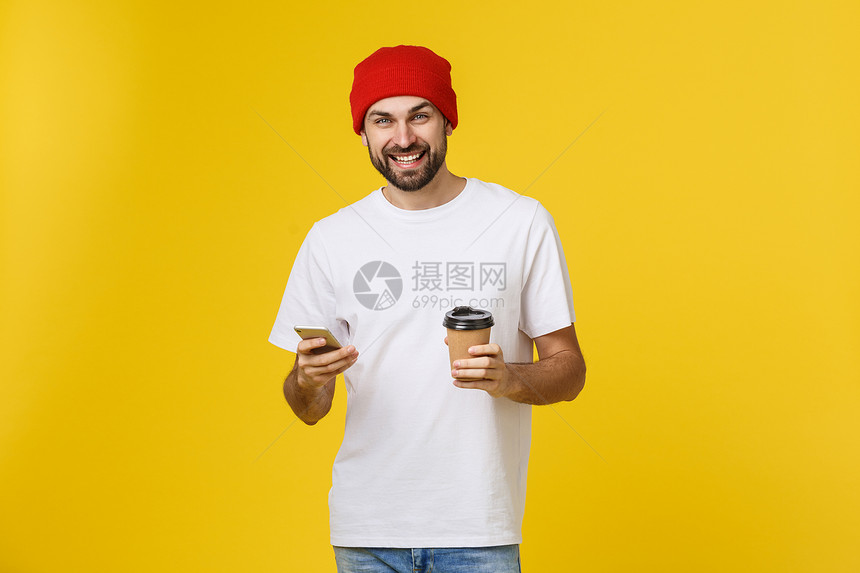 一位穿着便衣的快乐青年男子肖像身着便衣站在黄色背景之外拿着手机喝咖啡图片