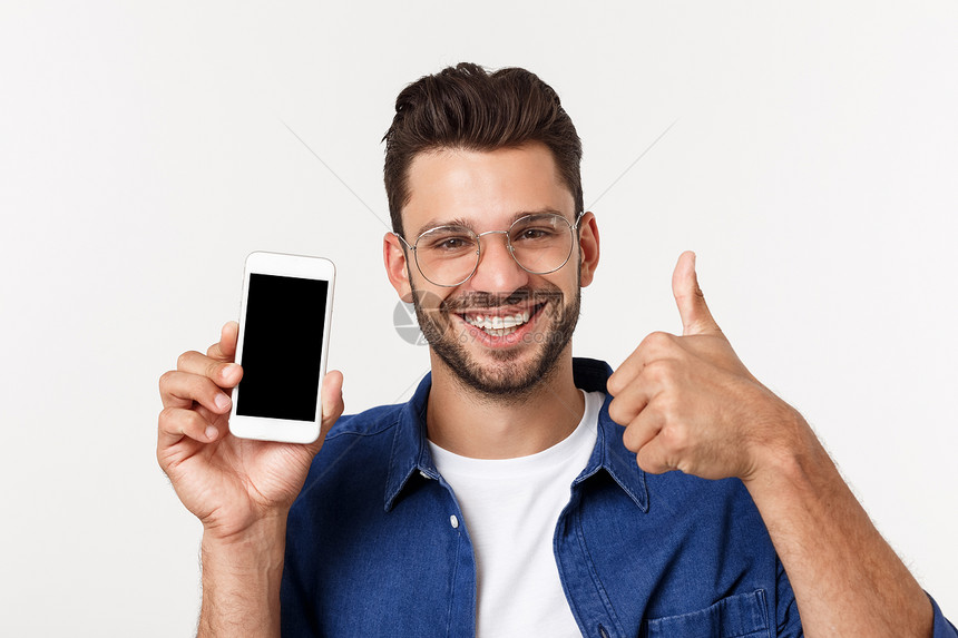 年轻男子显示一个空白的智能电话屏幕其拇指在白色背景上被隔离图片