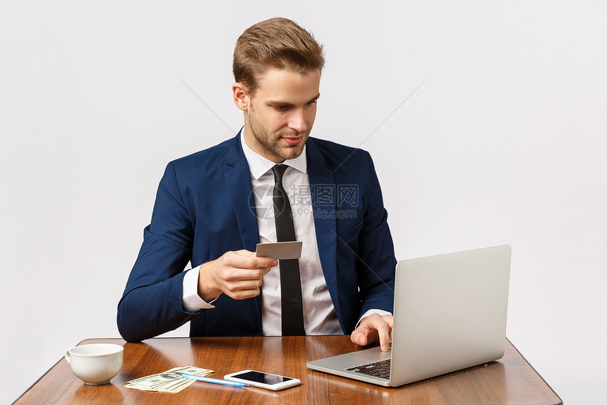 英俊的男在传统西装上坐在办公室想要给女朋友惊喜在网上商店订货持有信用卡在笔记本电脑上插入银行号码商业企家和工作概念英俊的男在传统图片