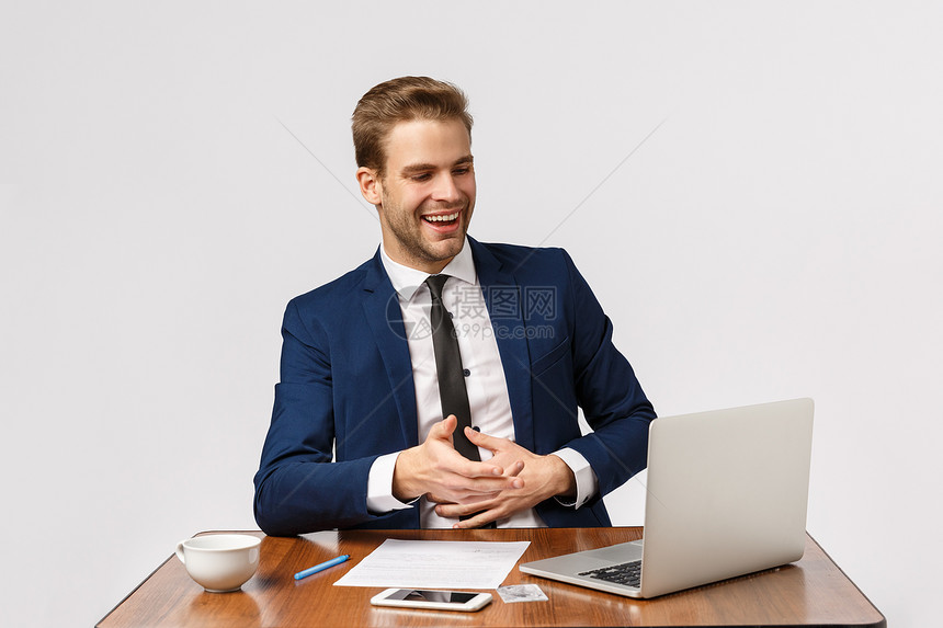 坐在办公室的有吸引力老板在笔记本电脑显示中嘲笑mes穿着西装休息白背景的英俊商人多么有趣的节目穿着西装白背景的英俊商人在工作图片