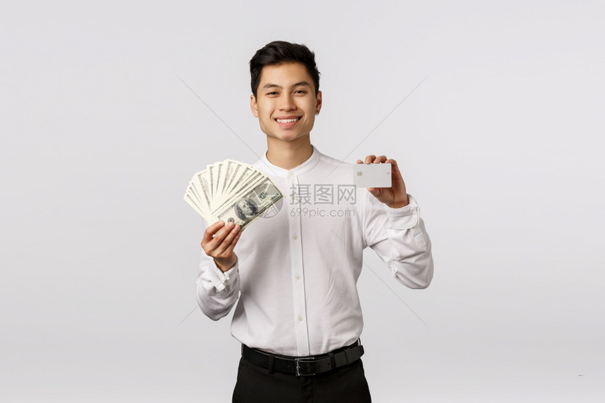 你更喜欢现金或卡片满足了英俊的亚洲商人持有金钱和白信用卡微笑着高兴有两个不同的支付方式富有站着白色背景您更喜欢的现金或卡片满足了图片