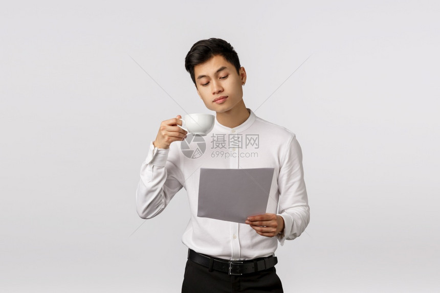 英俊的亚洲商人用杯子喝咖啡看文件阅读报告研究办公室工作的图表站立白人背景专横商业公司概念英俊的亚洲商人用杯子喝咖啡站立的白人背景图片