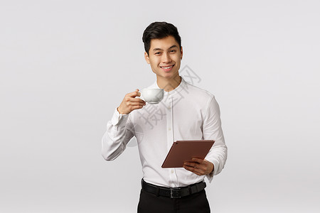 欢呼优雅的好相貌亚洲男子成功的企业家举起咖啡杯和微笑的喜悦持有数字平板电脑批准文件得到肯定的答复白色背景优雅的亚洲男子白色背景背景