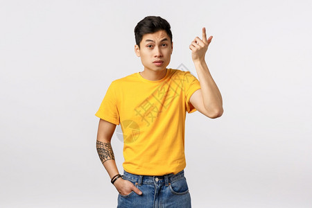 世界跆拳道联盟穿着黄色t恤衫的亚洲青年男子身穿黄色t恤纹身提高食用指惊慌和刺激举起眉毛如听胡言怪异对话白色背景wtf继续身穿黄色t恤衫惊慌和刺背景