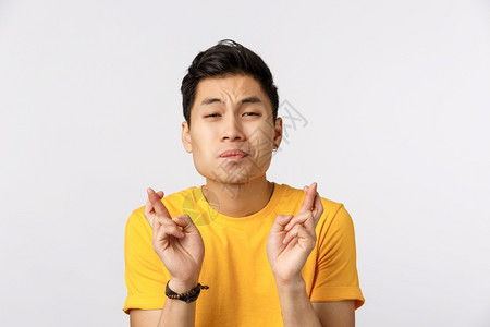 希望的年轻亚洲男子穿黄色t恤衫交叉手指好运求情面孔有强烈的愿望或梦想要的愿望成真期的希成真期待的美味和好交易请让它成真希望的年轻背景图片