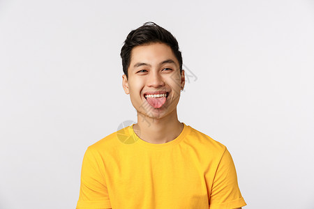 笑脸纹身素材穿着黄色t恤衫的有趣而快乐亚洲男子向外看和展示舌头制造笑脸玩耍积极情绪站在白色背景上快乐的白人男子穿着黄色t恤笑脸高兴和背景