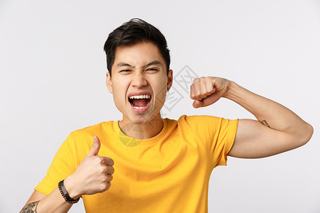 黄色大拇指穿着黄色t恤的勇敢自信和的亚洲男子展示肌肉和拇指高喊鼓励和兴奋欢呼鼓舞和兴奋背景