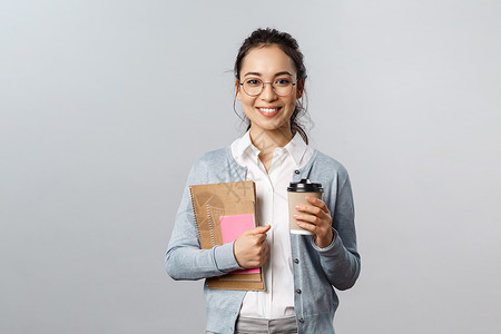 带着眼镜的女孩一只手抱着笔记本一只手拿着咖啡图片