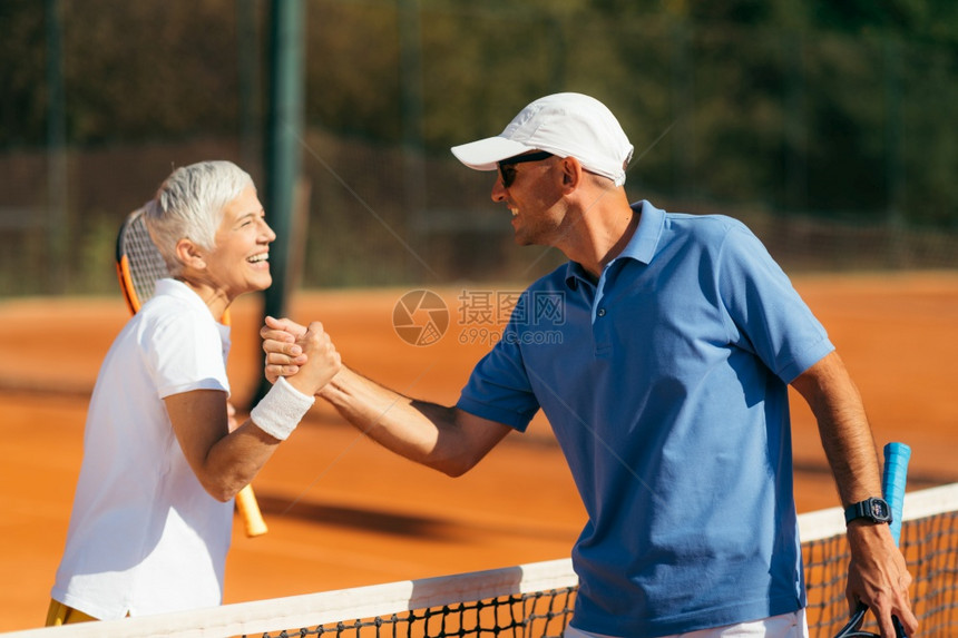 网球教练与60多岁高龄女握手在粘土场上网球课后握手图片