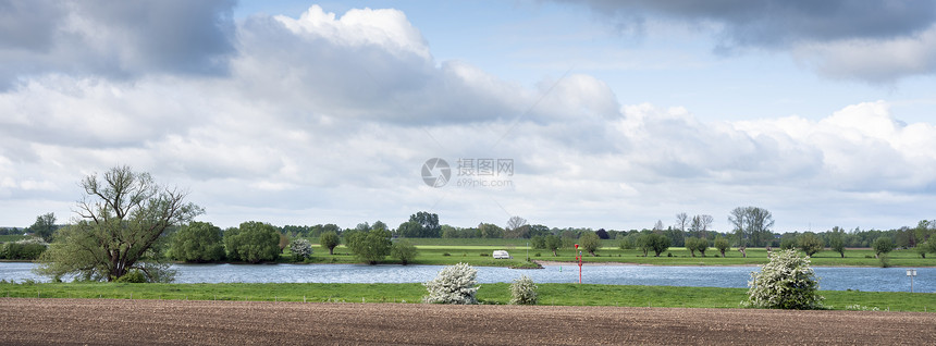 在阳光明媚的春天风景中开的树木和大篷车位于蓝天下云内河地带中央的列克河周围阳光明媚春风中图片