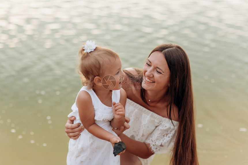 在湖边拥抱女儿暑假的概念母亲和婴儿和rday一起度过时间家庭看起来阳光照耀母亲在湖边的海滩上拥抱女儿暑假的概念母亲和婴图片