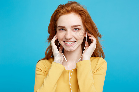 姜黄色头发快乐的姜红发女孩肖像喜欢听音乐耳机笑着看摄影机孤立在蓝面画背景上复制空间背景
