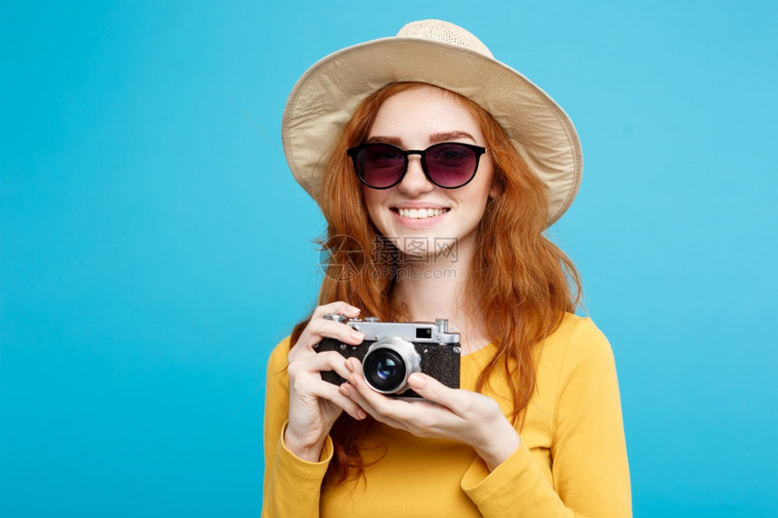 旅行概念关闭肖像年轻漂亮的红头发女孩戴着时尚帽子太阳镜和古董相机微笑在镜头面前图片
