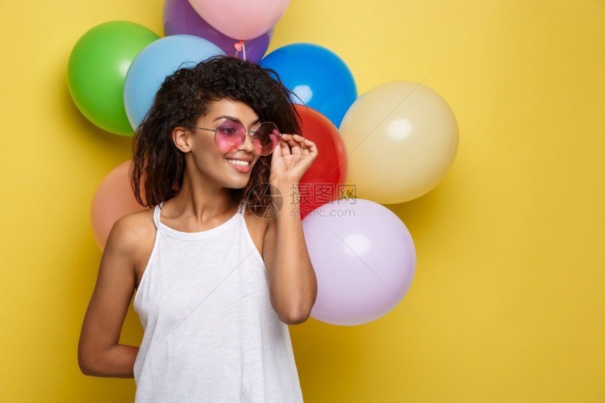 庆祝概念关闭快乐的年轻非洲美女肖像穿着白色t恤带彩派对气球微笑的白色t恤黄的面糊工作室背景关闭快乐的年轻美丽非洲女肖像黄色的面糊图片