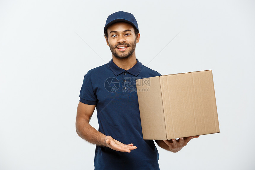 交付概念快乐的非洲送货员肖像指向展示一个盒子包孤立在灰色工作室背景上复制空间图片