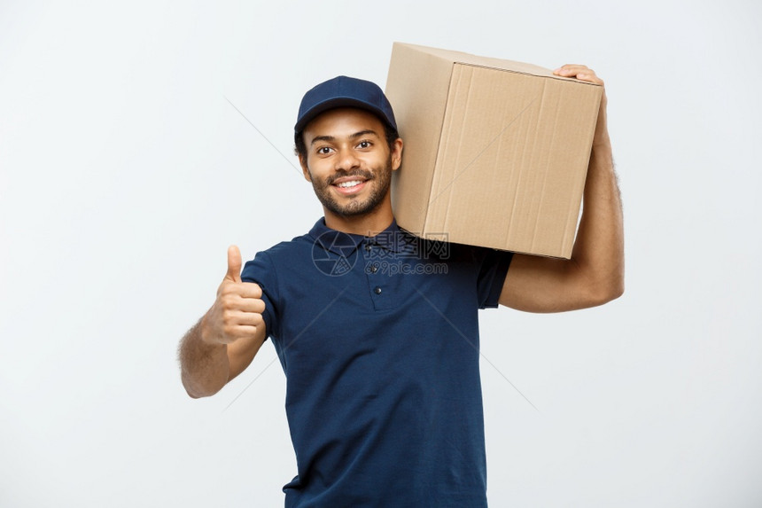 交付概念快乐的非洲送货员肖像他拿着一个盒子包并展示出震动孤立在灰色工作室背景上复制空间快乐的非洲送货员肖像显示震动复制空间图片