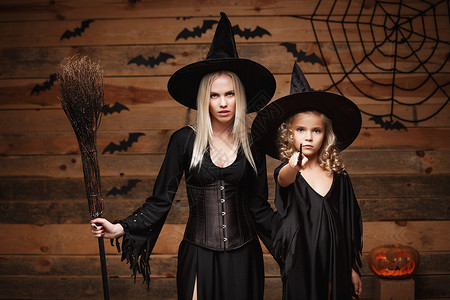 巫家坝halowen概念快乐的母亲和女儿穿着巫服庆祝halowen装扮有弯曲南瓜的圣殿在木制工作室背景上的蝙蝠和蜘蛛网之上打扮成弯曲南背景