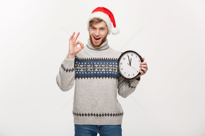 假期概念年轻英俊的胡子男穿着毛衣白色时钟给好牌图片