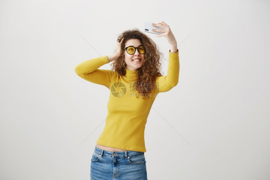 迷人的时髦女在智能手机上拍自白色背景的自拍图片