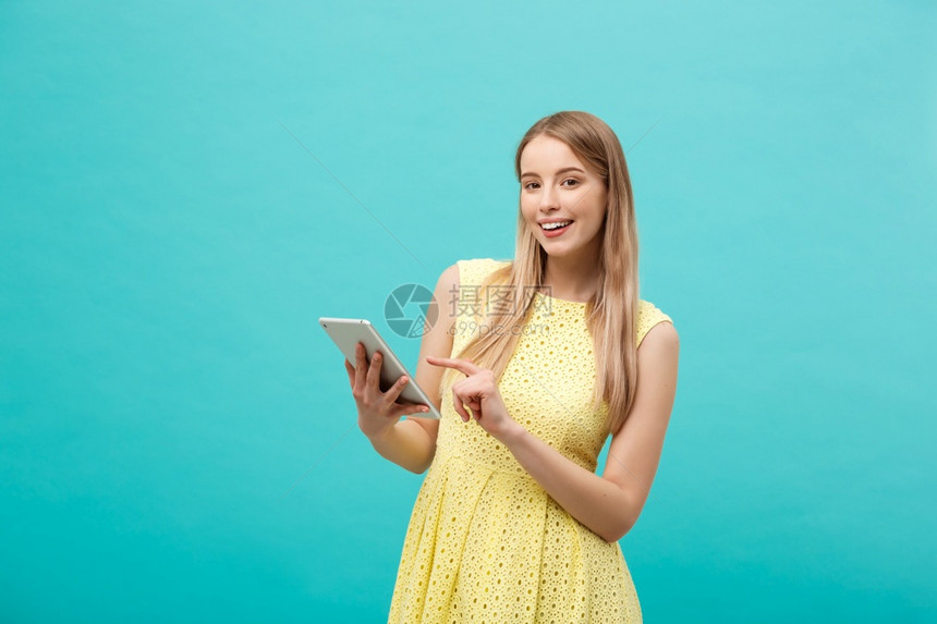 一位年轻快乐女肖像她拿着带复制空间的平板电脑站在蓝色背景的隔离处一位年轻快乐女肖像拿着带复制空间的平板电脑站在蓝色背景的隔离处图片
