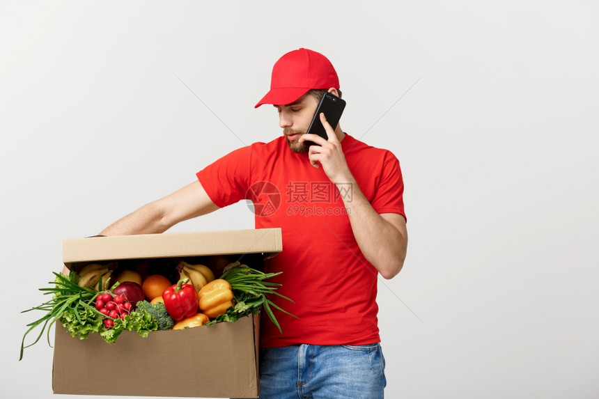 送货员拿着纸箱带食物用手机打电话隔着灰色背景送货员拿着纸箱隔灰色背景图片