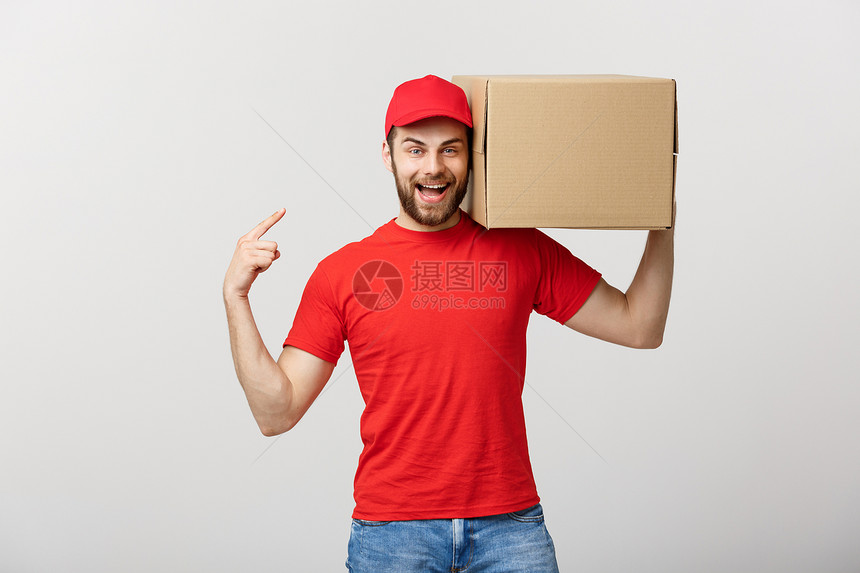 交付概念愉快的天主送货员的肖像手指着一个盒子包孤立在灰色工作室背景上复制空间快乐的天主送货员的肖像孤立在灰色工作室背景上复制空间图片