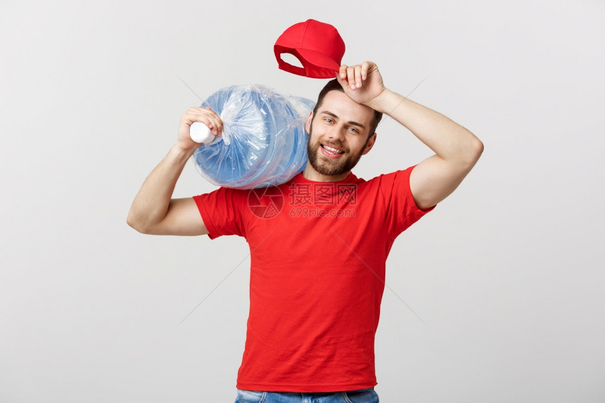 交付概念笑瓶装水运送快递员用红色t恤衫和帽子装满图片