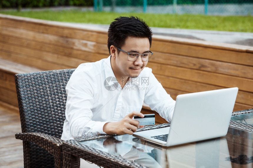 英俊的青年男子享受用信卡在移动电话上购物的乐趣图片